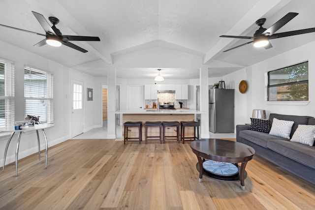 living area featuring baseboards, lofted ceiling with beams, a ceiling fan, and light wood-style floors