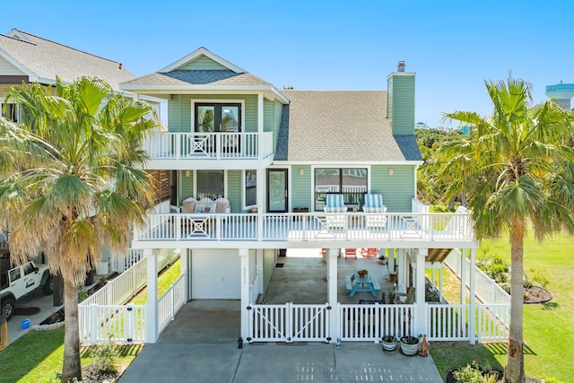 22317 Isle View Dr, Galveston, TX 77554 - rear view of house with a balcony, a gate, a chimney, a garage, and roof with shingles