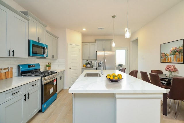 kitchen with light countertops, visible vents, stainless steel appliances, a sink, and backsplash