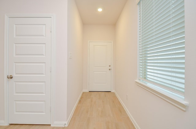 hallway featuring baseboards, light wood finished floors, and recessed lighting