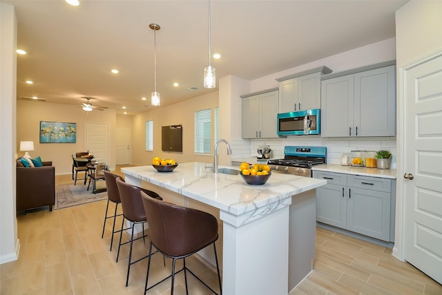 kitchen featuring tasteful backsplash, stainless steel appliances, gray cabinetry, a breakfast bar, and a sink