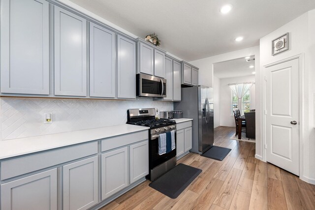 kitchen featuring stainless steel appliances, gray cabinets, decorative backsplash, light wood-type flooring, and recessed lighting