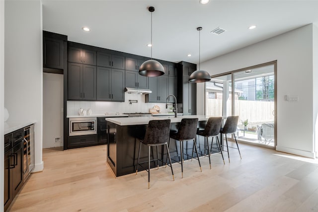 kitchen featuring light countertops, tasteful backsplash, under cabinet range hood, stainless steel appliances, and visible vents