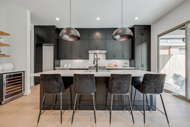 kitchen with light countertops, tasteful backsplash, beverage cooler, light wood-style flooring, and under cabinet range hood