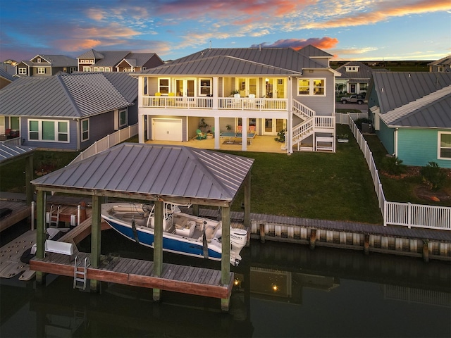 back of house featuring a standing seam roof, metal roof, boat lift, a lawn, and a water view