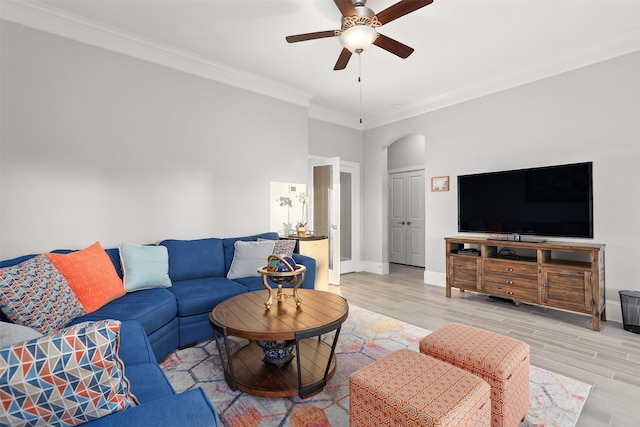 living room featuring arched walkways, ornamental molding, light wood-style flooring, and a ceiling fan