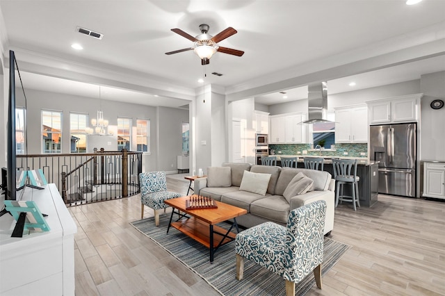 living room with ceiling fan with notable chandelier, light wood finished floors, and visible vents