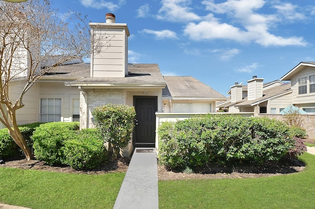 view of front facade with a chimney, a front yard, and roof with shingles