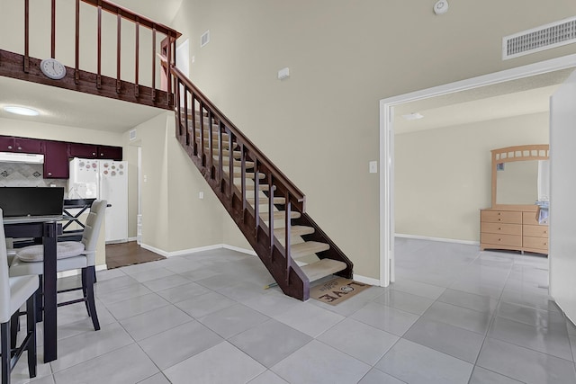 stairway with a towering ceiling, visible vents, and tile patterned flooring