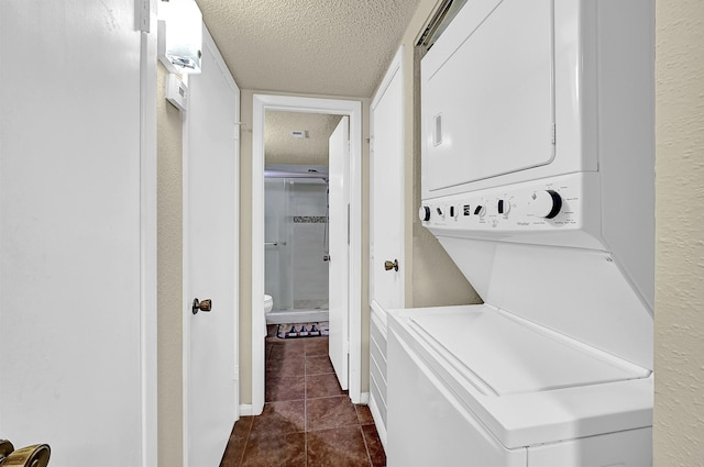 clothes washing area with stacked washer and clothes dryer, dark tile patterned flooring, and a textured ceiling