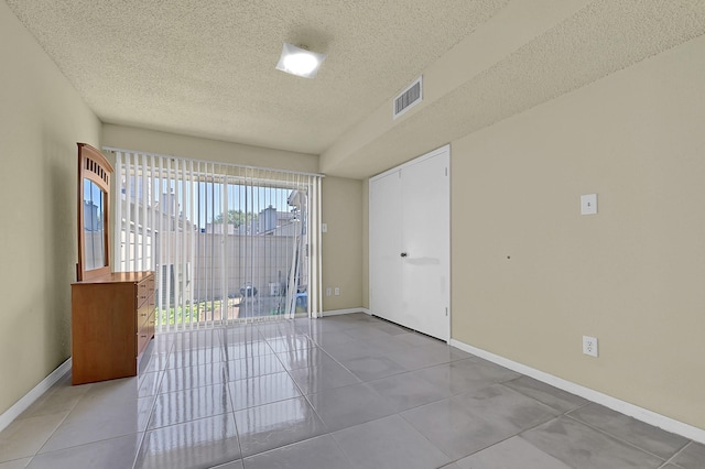 unfurnished room with light tile patterned floors, a textured ceiling, baseboards, and visible vents