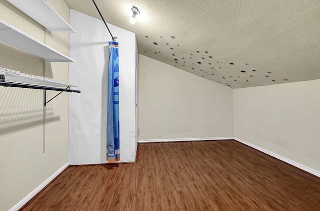 additional living space with baseboards, a textured ceiling, wood finished floors, and vaulted ceiling