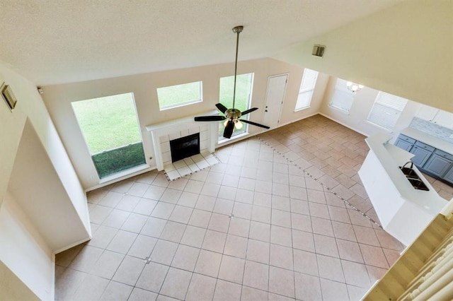 unfurnished living room with visible vents, a tiled fireplace, a ceiling fan, vaulted ceiling, and light tile patterned floors