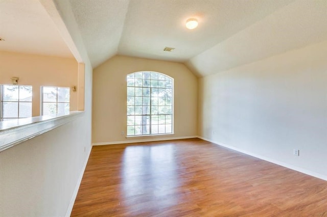spare room with a textured ceiling, visible vents, baseboards, wood finished floors, and lofted ceiling