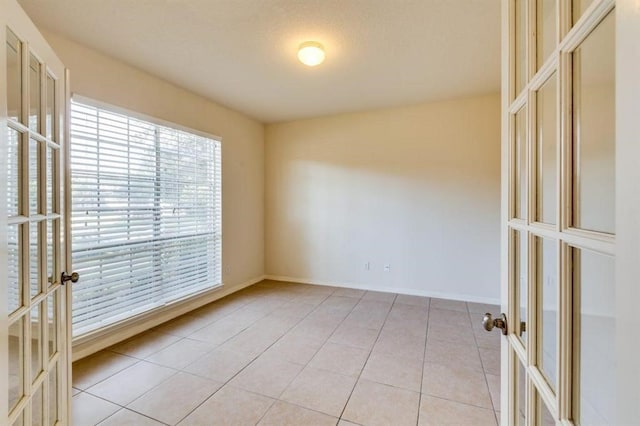 spare room featuring light tile patterned flooring, baseboards, and french doors