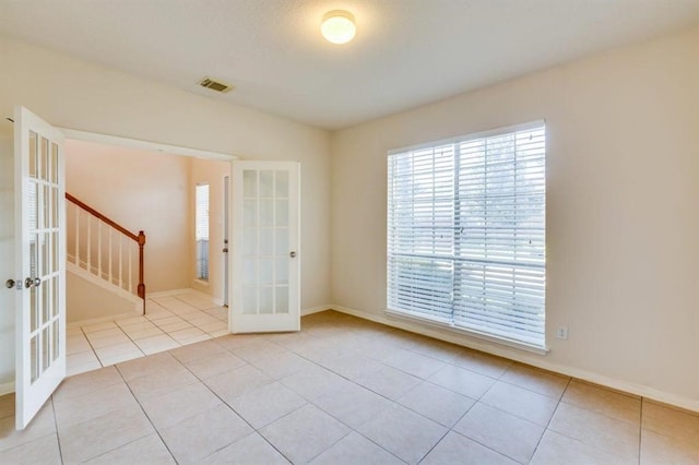 tiled spare room featuring baseboards, visible vents, stairway, and french doors