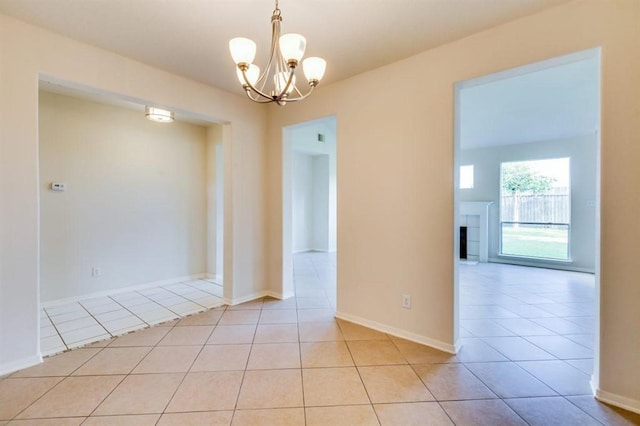 empty room with baseboards, a tile fireplace, an inviting chandelier, and light tile patterned floors