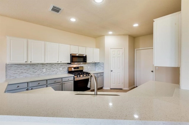 kitchen with stainless steel appliances, decorative backsplash, light stone counters, visible vents, and white cabinets