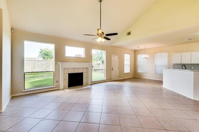 unfurnished living room with light tile patterned floors, ceiling fan with notable chandelier, baseboards, visible vents, and a tiled fireplace