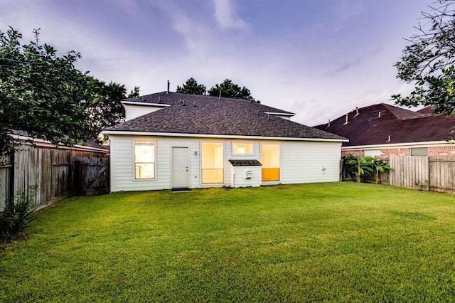 back of house with a fenced backyard, roof with shingles, and a yard