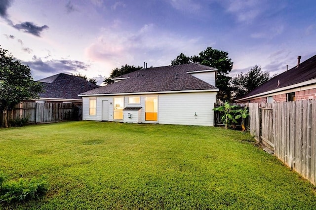back of property with a fenced backyard, a shingled roof, and a yard