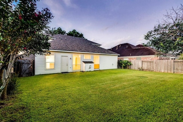 back of house at dusk featuring a fenced backyard, roof with shingles, and a yard