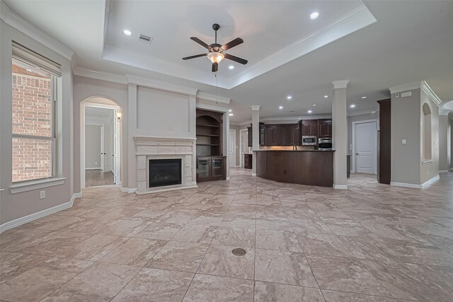 4210 Wentworth Dr, Fulshear, TX 77441 - unfurnished living room with a tray ceiling, ceiling fan, arched walkways, decorative columns, and a glass covered fireplace
