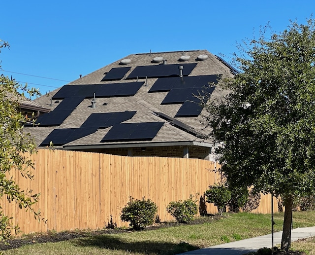 view of home's exterior featuring fence, roof mounted solar panels, and roof with shingles