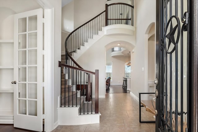 foyer with tile patterned floors, stairway, a high ceiling, baseboards, and arched walkways