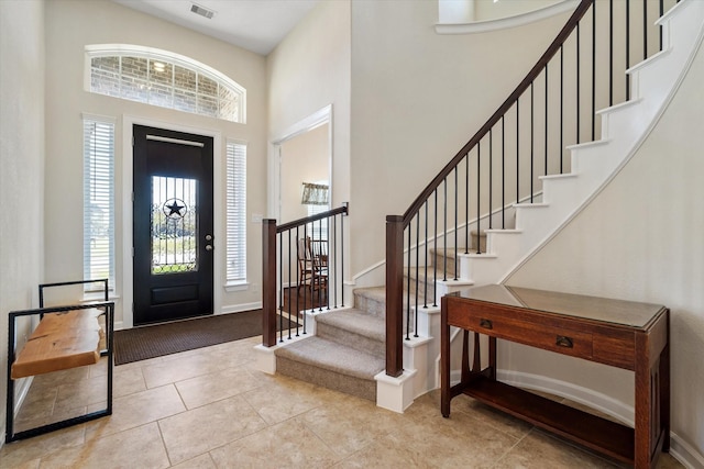 tiled foyer featuring stairs, visible vents, a towering ceiling, and baseboards