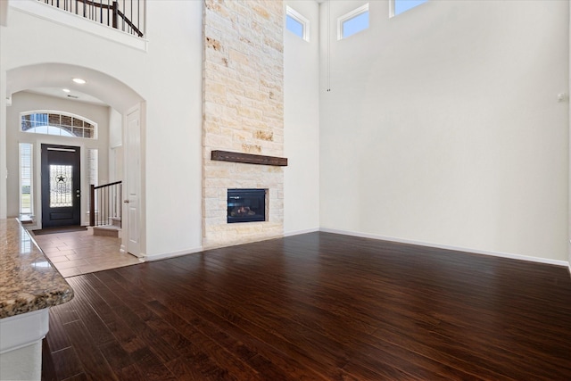 unfurnished living room featuring a wealth of natural light, a towering ceiling, and dark wood finished floors