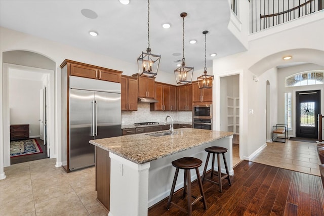 kitchen with decorative backsplash, arched walkways, under cabinet range hood, a sink, and built in appliances