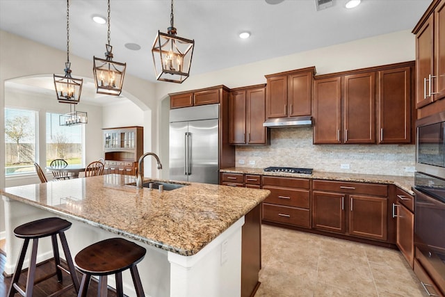 kitchen with built in appliances, arched walkways, under cabinet range hood, and a sink