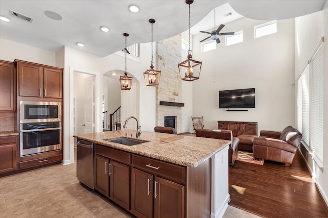 kitchen with a sink, a stone fireplace, stainless steel appliances, visible vents, and ceiling fan
