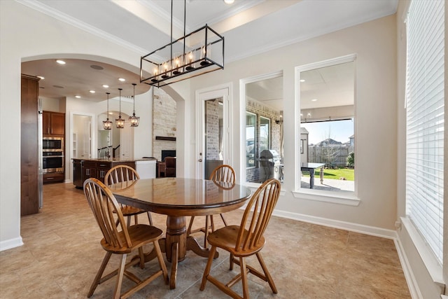 dining space featuring arched walkways, a fireplace, an inviting chandelier, and crown molding