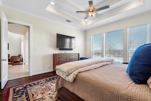 bedroom featuring crown molding, a raised ceiling, wood finished floors, baseboards, and visible vents