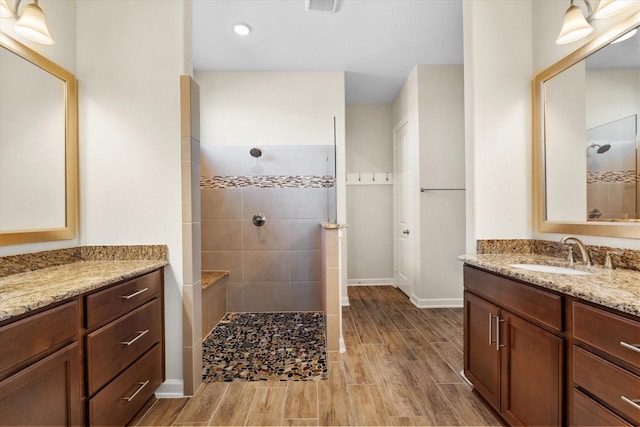 bathroom featuring wood tiled floor, two vanities, a sink, and walk in shower