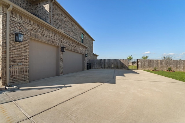 view of home's exterior featuring brick siding, concrete driveway, a gate, and fence