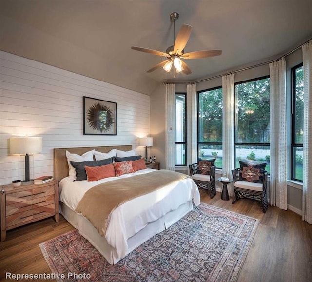 bedroom with a ceiling fan, wood walls, and wood finished floors