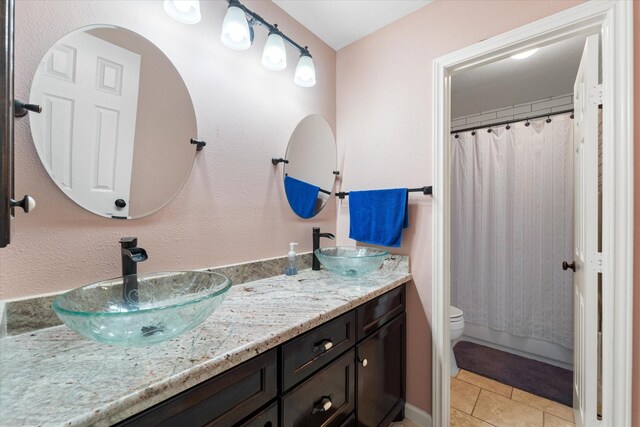 full bath with toilet, tile patterned flooring, a sink, and double vanity