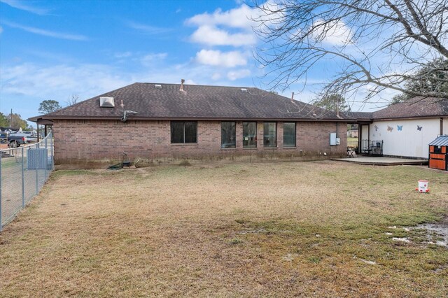 rear view of property with roof with shingles, fence, brick siding, a patio, and a lawn