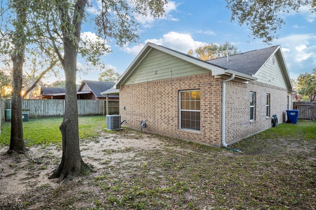 rear view of house with brick siding, central AC unit, a fenced backyard, and a yard