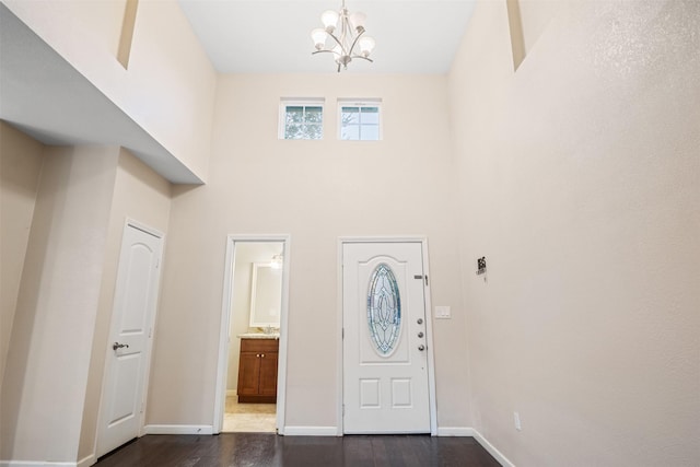 foyer entrance featuring dark wood-style flooring, a towering ceiling, baseboards, and a chandelier