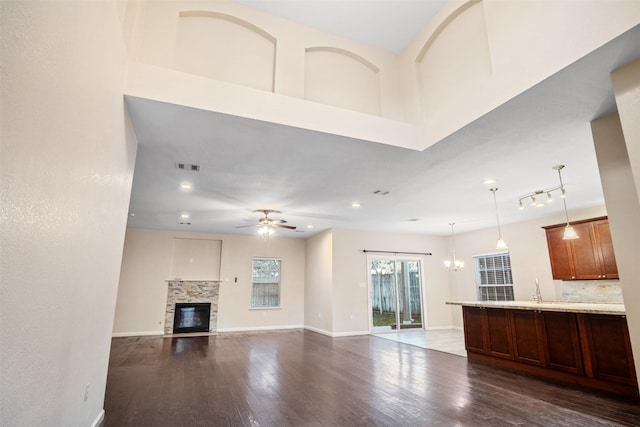 unfurnished living room featuring dark wood-style flooring, baseboards, visible vents, a glass covered fireplace, and ceiling fan