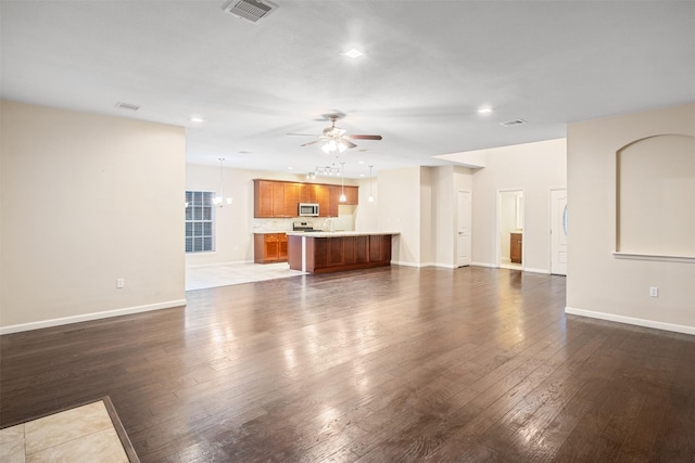 unfurnished living room with ceiling fan with notable chandelier, visible vents, baseboards, and dark wood-style floors