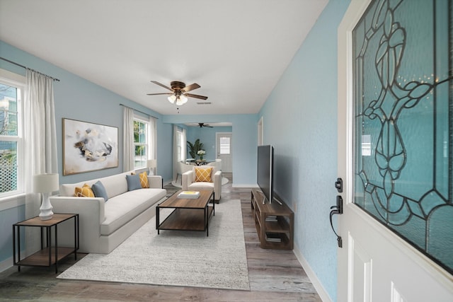 living area with baseboards, a ceiling fan, and wood finished floors
