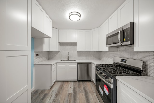 kitchen featuring a sink, light wood finished floors, a textured ceiling, stainless steel appliances, and decorative backsplash
