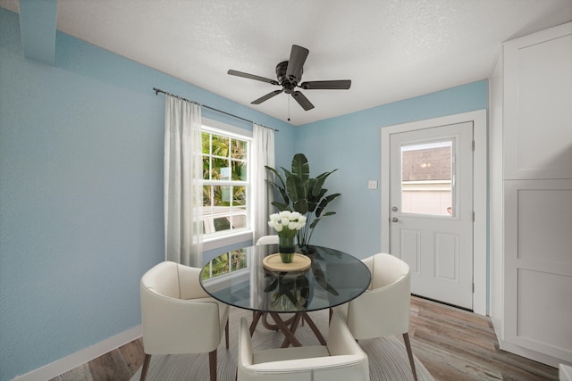 dining room with baseboards, a ceiling fan, light wood-type flooring, and a textured ceiling