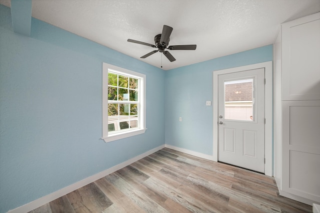 unfurnished room featuring baseboards, ceiling fan, light wood finished floors, and a textured ceiling