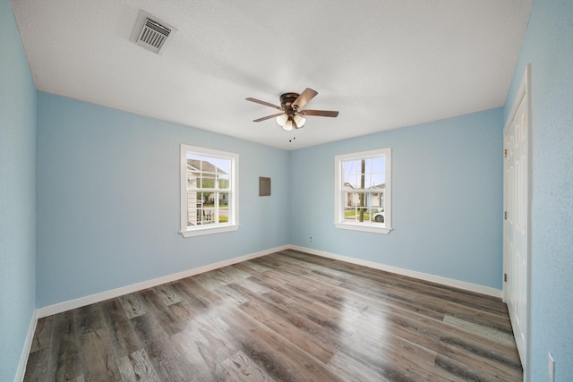 unfurnished room featuring wood finished floors, plenty of natural light, ceiling fan, and visible vents